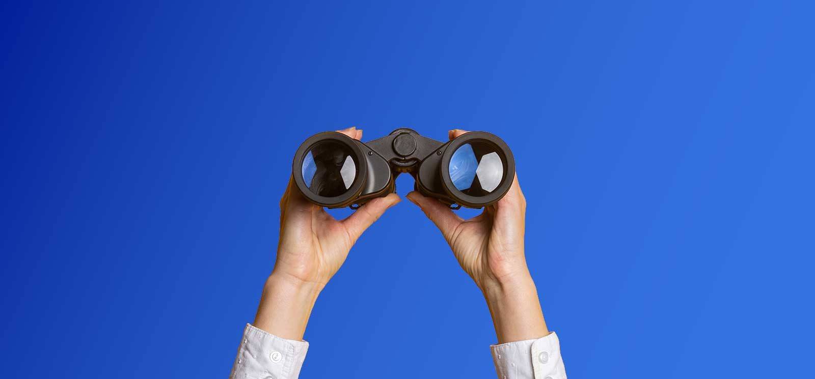 Woman holding binoculars on blue background.